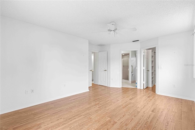 unfurnished bedroom with a textured ceiling, a walk in closet, a closet, light hardwood / wood-style floors, and ceiling fan