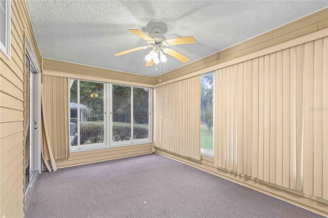 carpeted spare room featuring a textured ceiling, ceiling fan, and wooden walls