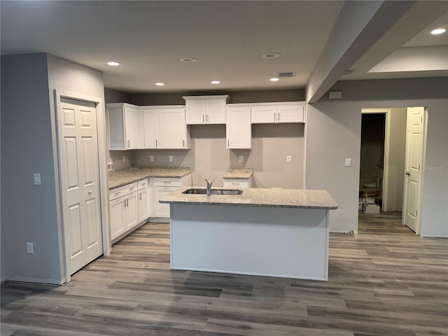 kitchen featuring white cabinets, light stone countertops, a center island with sink, and dark hardwood / wood-style flooring