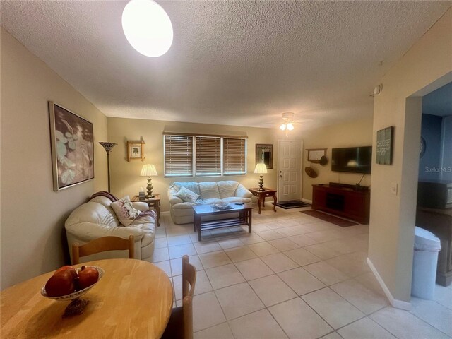 living room with a textured ceiling, ceiling fan, and light tile patterned floors