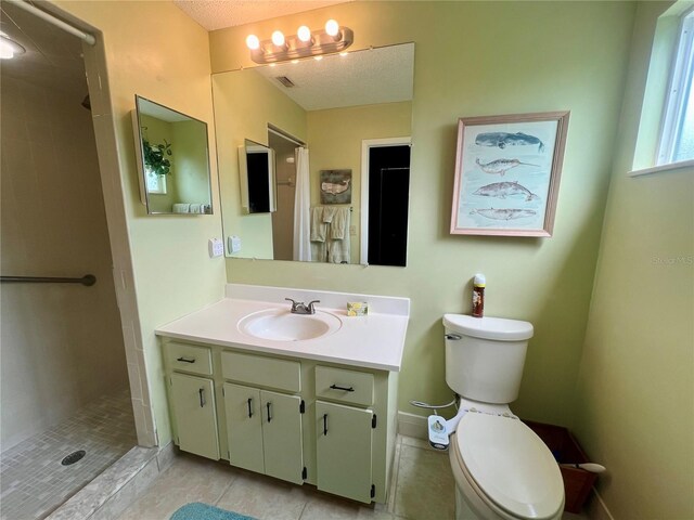 bathroom with tile patterned flooring, a textured ceiling, tiled shower, vanity, and toilet