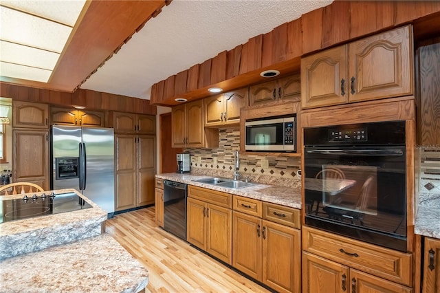 kitchen featuring light stone counters, backsplash, light wood-type flooring, black appliances, and sink