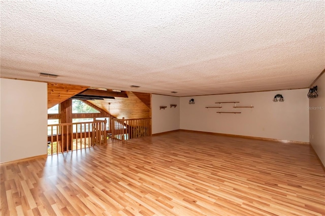 additional living space with wooden walls, light hardwood / wood-style flooring, and a textured ceiling