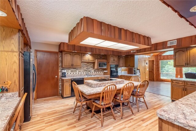 kitchen featuring an island with sink, light hardwood / wood-style flooring, a breakfast bar, and black appliances