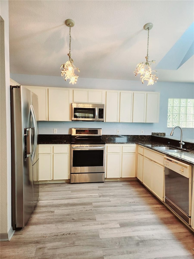 kitchen featuring cream cabinets, a sink, hanging light fixtures, appliances with stainless steel finishes, and dark countertops