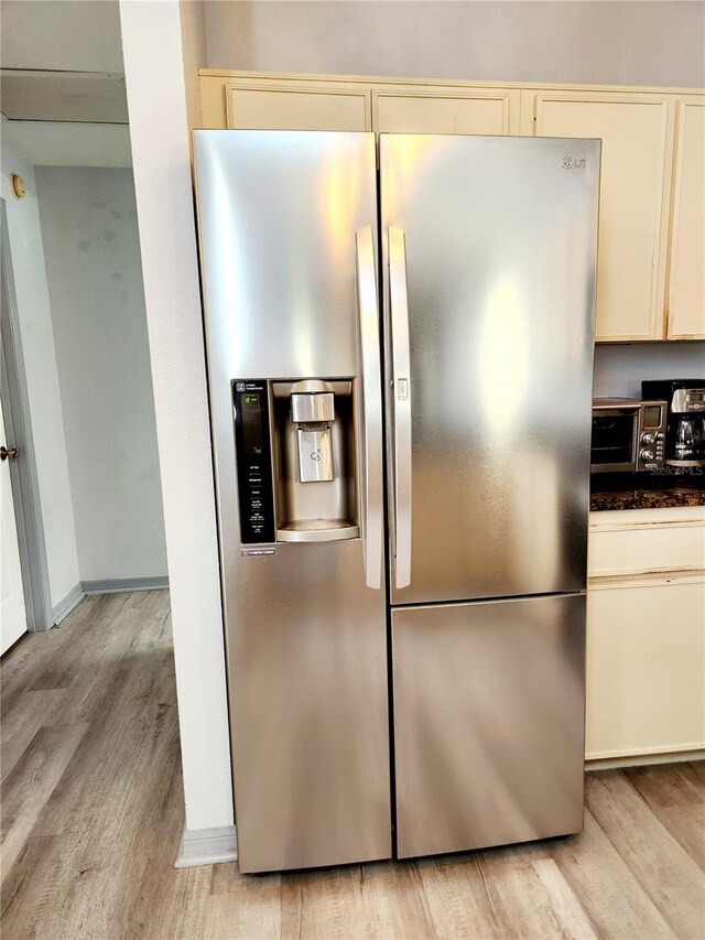 interior details featuring dark countertops, light wood-style floors, stainless steel refrigerator with ice dispenser, and cream cabinetry