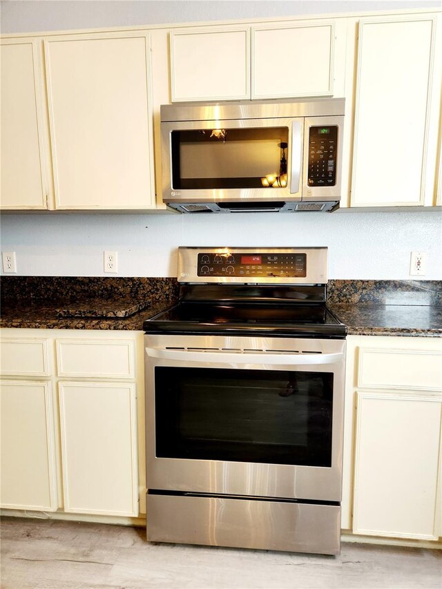 kitchen with dark stone counters, appliances with stainless steel finishes, and cream cabinets