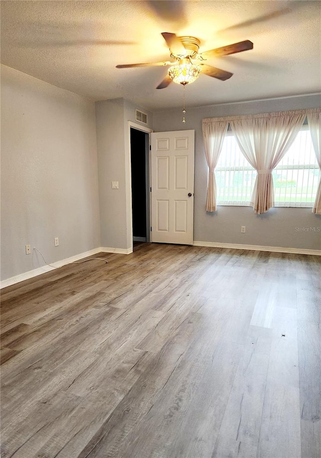 spare room featuring a textured ceiling, wood finished floors, a ceiling fan, visible vents, and baseboards