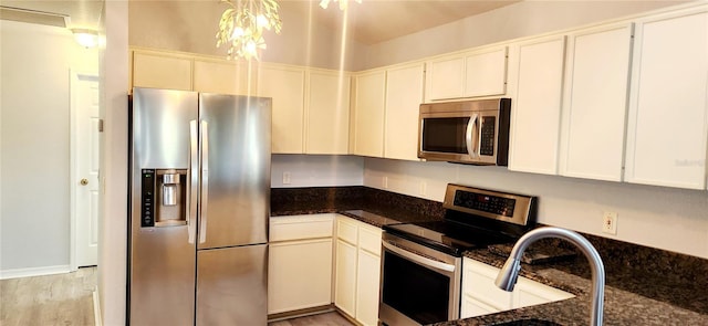 17808 SE 115th Ct, Summerfield, FL 34491 - kitchen with appliances with stainless steel finishes, dark stone counters, light wood finished floors, and white cabinetry