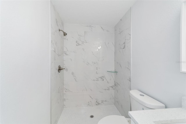 bathroom with toilet, a tile shower, and vanity