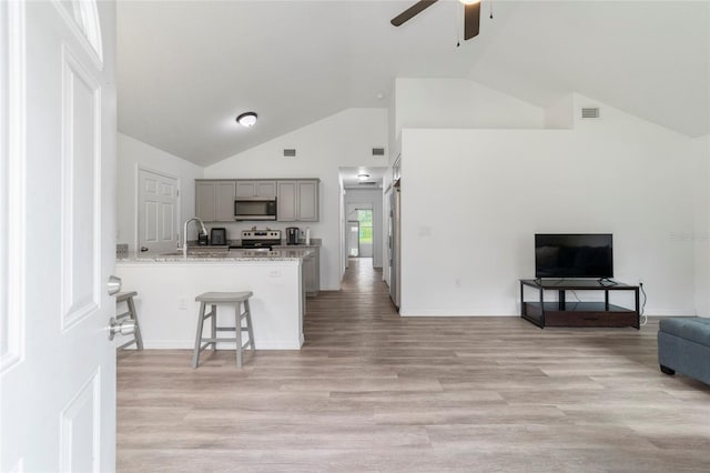 kitchen featuring stainless steel appliances, kitchen peninsula, light stone counters, ceiling fan, and gray cabinetry