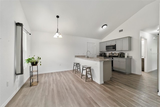 kitchen with gray cabinetry, hanging light fixtures, light wood-type flooring, light stone counters, and stainless steel appliances