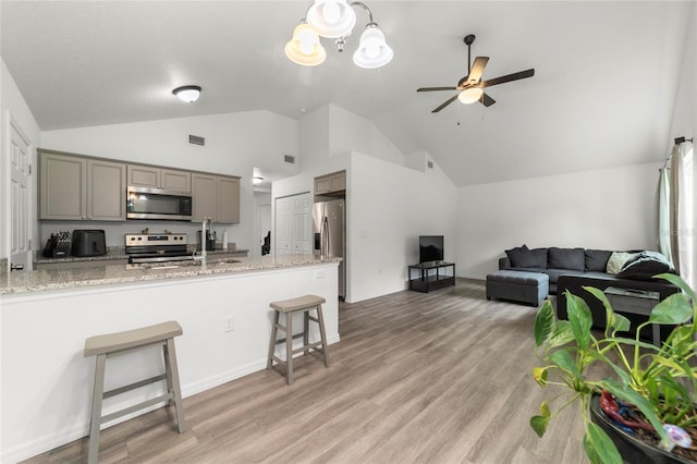 kitchen featuring a kitchen bar, light stone countertops, ceiling fan, appliances with stainless steel finishes, and light hardwood / wood-style floors