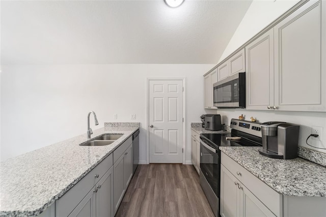 kitchen with vaulted ceiling, appliances with stainless steel finishes, dark hardwood / wood-style flooring, sink, and gray cabinets