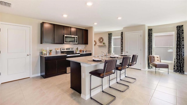 kitchen with appliances with stainless steel finishes, a breakfast bar, a center island with sink, and light tile patterned flooring