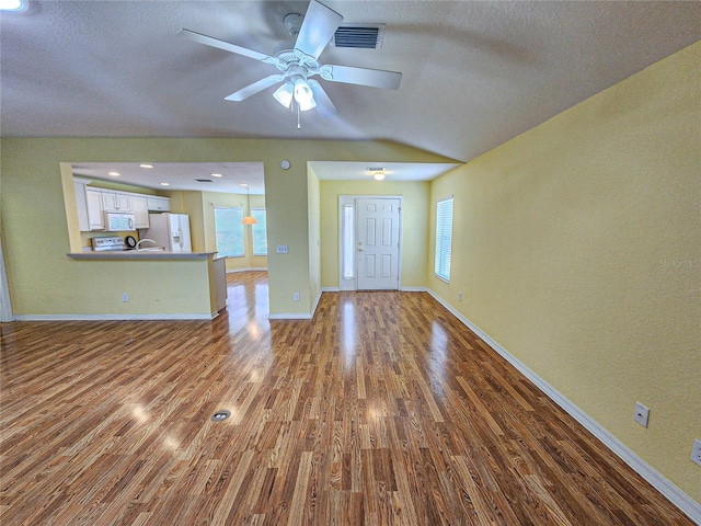 unfurnished living room with a wealth of natural light, vaulted ceiling, ceiling fan, and hardwood / wood-style floors