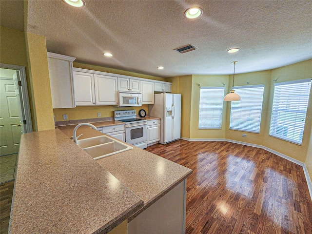 kitchen with dark hardwood / wood-style flooring, white appliances, kitchen peninsula, and sink