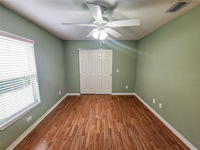 unfurnished bedroom with wood-type flooring, multiple windows, ceiling fan, and a textured ceiling