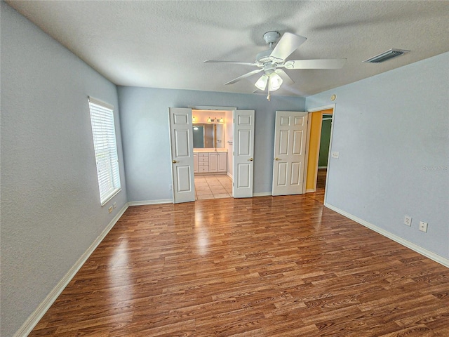 unfurnished bedroom featuring ceiling fan, hardwood / wood-style flooring, ensuite bathroom, and a textured ceiling