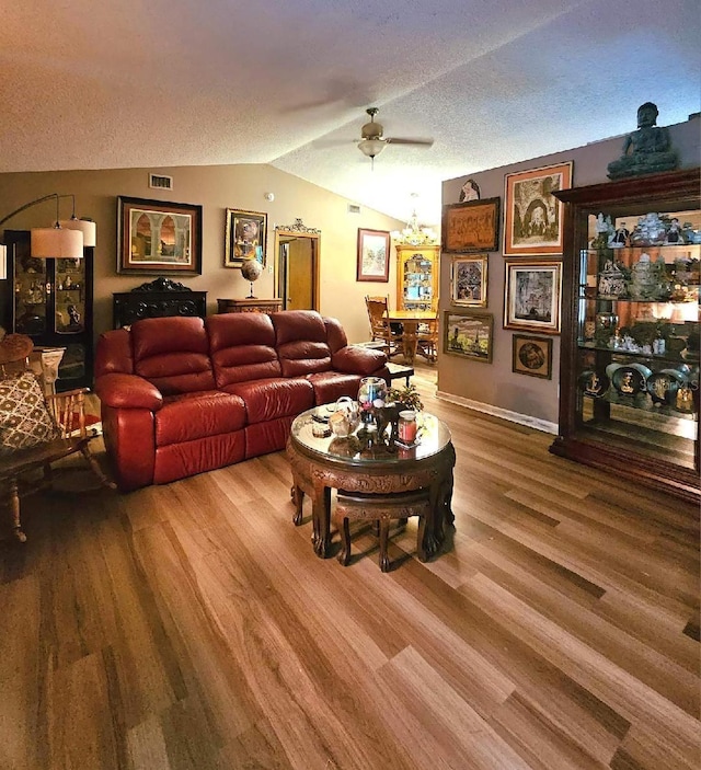 living room featuring wood-type flooring, ceiling fan with notable chandelier, a textured ceiling, and lofted ceiling