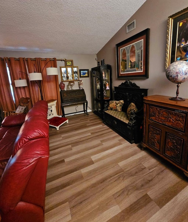 living room featuring a textured ceiling, light wood-type flooring, and lofted ceiling