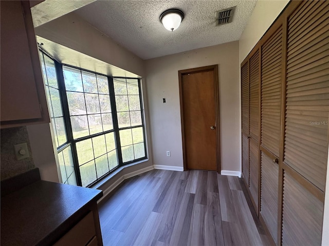 unfurnished bedroom featuring visible vents, a textured ceiling, a closet, baseboards, and dark wood-style flooring