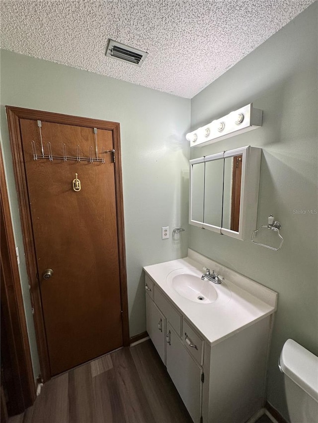 bathroom with visible vents, toilet, vanity, wood finished floors, and a textured ceiling