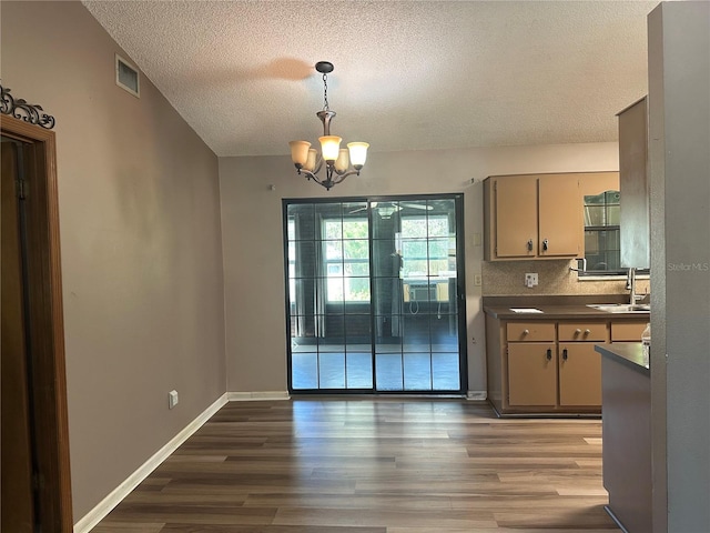 unfurnished dining area featuring visible vents, a chandelier, lofted ceiling, wood finished floors, and a sink