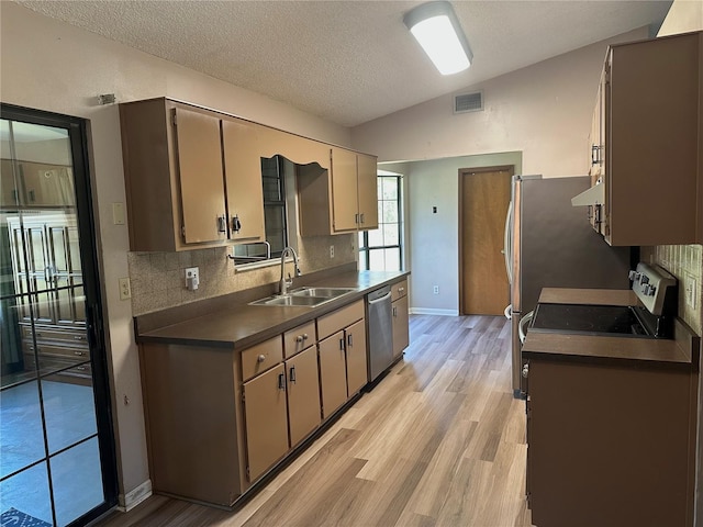 kitchen featuring visible vents, lofted ceiling, a sink, stainless steel appliances, and dark countertops