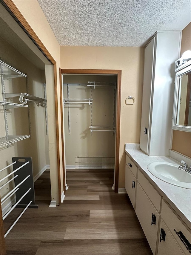 bathroom with baseboards, a textured ceiling, wood finished floors, and vanity