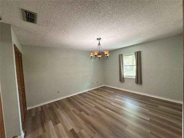 unfurnished room featuring visible vents, baseboards, a chandelier, wood finished floors, and a textured ceiling