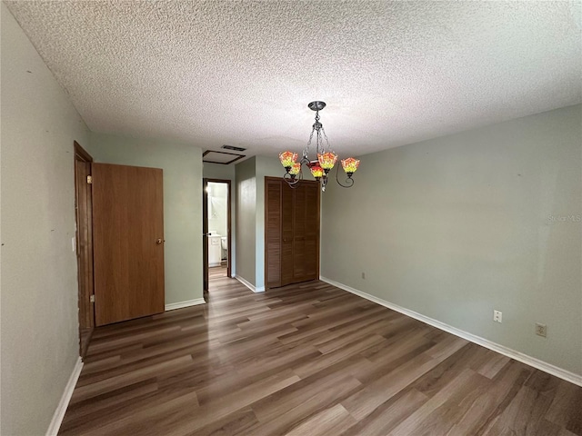 spare room featuring visible vents, baseboards, a chandelier, wood finished floors, and a textured ceiling