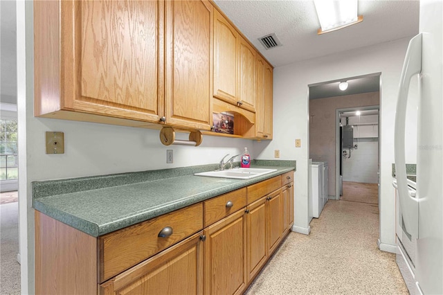 kitchen featuring white fridge, sink, a textured ceiling, and washer and clothes dryer