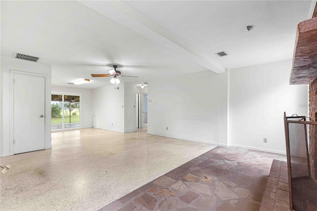 empty room with beam ceiling, a brick fireplace, a textured ceiling, and ceiling fan