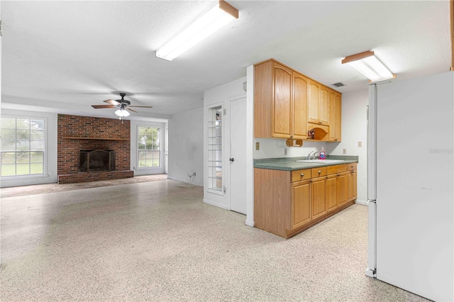 kitchen with sink, a brick fireplace, a textured ceiling, white refrigerator, and ceiling fan