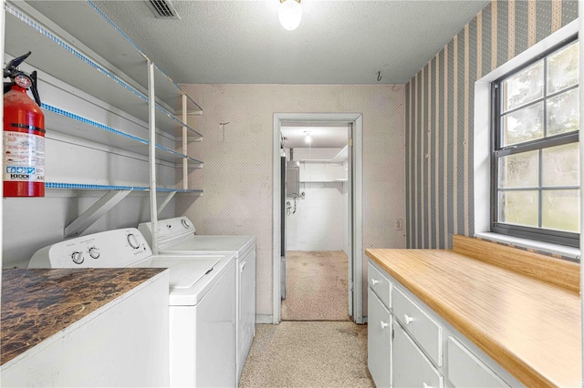 washroom with cabinets, washing machine and clothes dryer, a textured ceiling, and a wealth of natural light