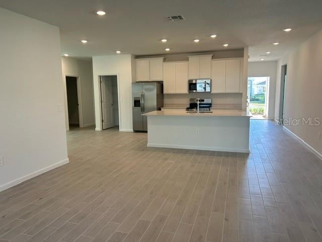 kitchen featuring white cabinetry, a center island with sink, stainless steel appliances, and light hardwood / wood-style floors