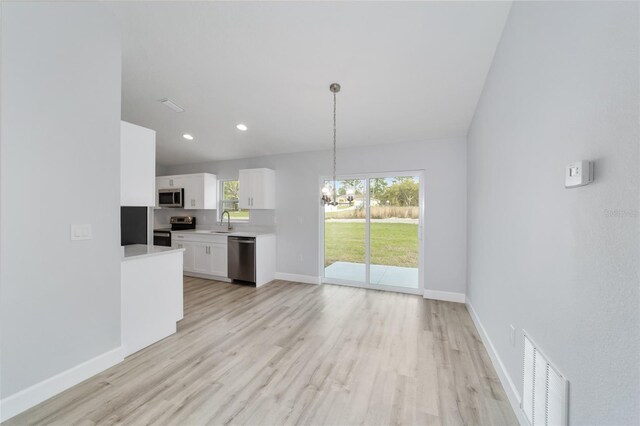 kitchen with white cabinets, light wood-type flooring, decorative light fixtures, and stainless steel appliances