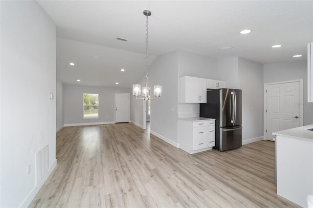 kitchen with white cabinets, hanging light fixtures, light hardwood / wood-style flooring, an inviting chandelier, and stainless steel fridge