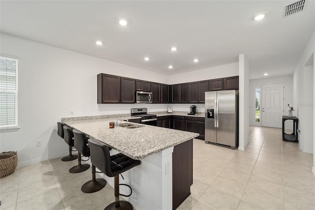 kitchen with appliances with stainless steel finishes, a breakfast bar, kitchen peninsula, light stone countertops, and sink