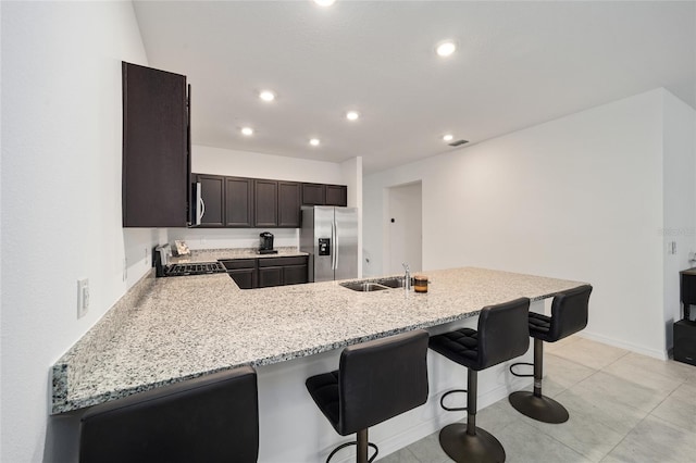 kitchen with sink, kitchen peninsula, stainless steel appliances, a kitchen breakfast bar, and light stone countertops