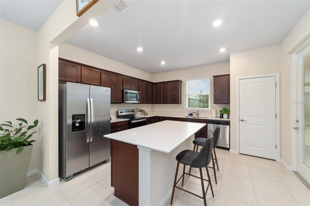 kitchen with dark brown cabinetry, light tile patterned flooring, a kitchen island, stainless steel appliances, and a breakfast bar