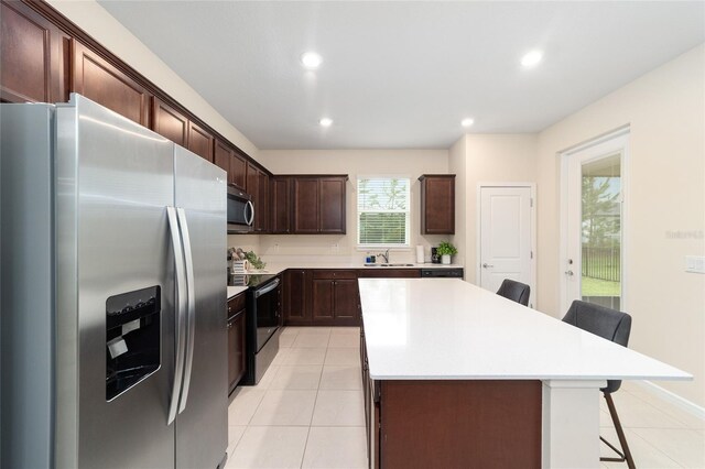 kitchen with appliances with stainless steel finishes, light tile patterned flooring, a center island, and a kitchen breakfast bar