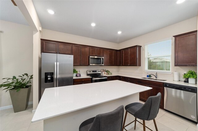 kitchen with a breakfast bar area, sink, a kitchen island, appliances with stainless steel finishes, and light tile patterned floors