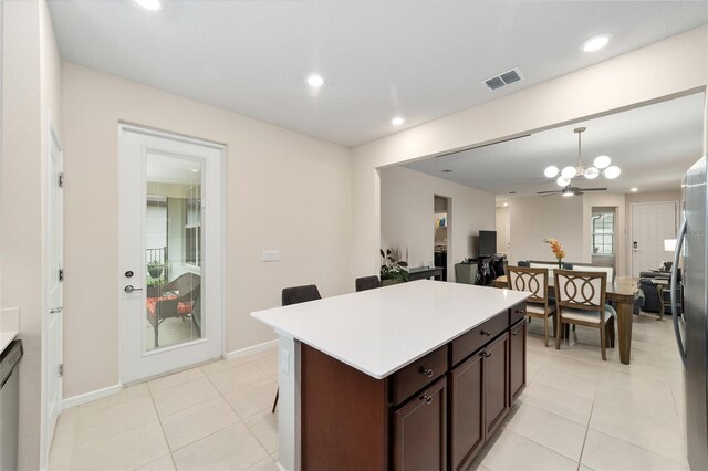 kitchen with hanging light fixtures, light tile patterned floors, a kitchen island, dark brown cabinets, and ceiling fan with notable chandelier