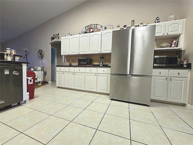 kitchen featuring appliances with stainless steel finishes, light tile patterned floors, white cabinetry, and vaulted ceiling