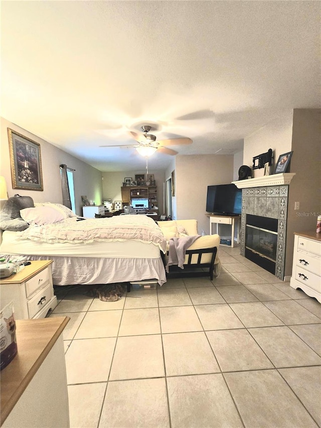 bedroom with ceiling fan, light tile patterned floors, a textured ceiling, and a tile fireplace