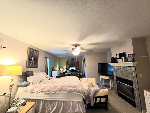 bedroom with ceiling fan, light tile patterned floors, a textured ceiling, and a tile fireplace