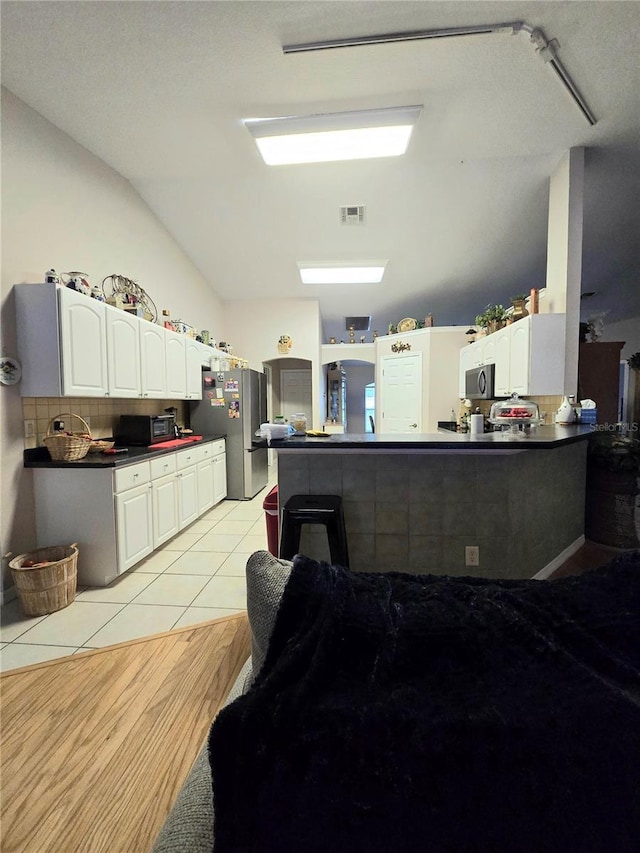 kitchen featuring kitchen peninsula, stainless steel appliances, vaulted ceiling, white cabinetry, and light tile patterned flooring