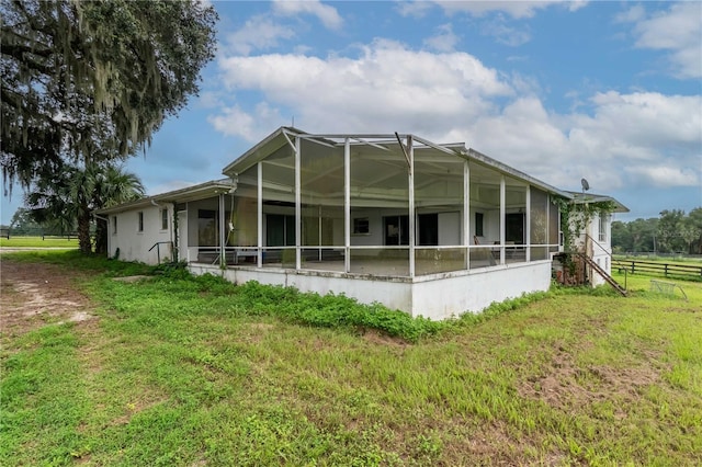 back of property with a sunroom, a yard, and glass enclosure